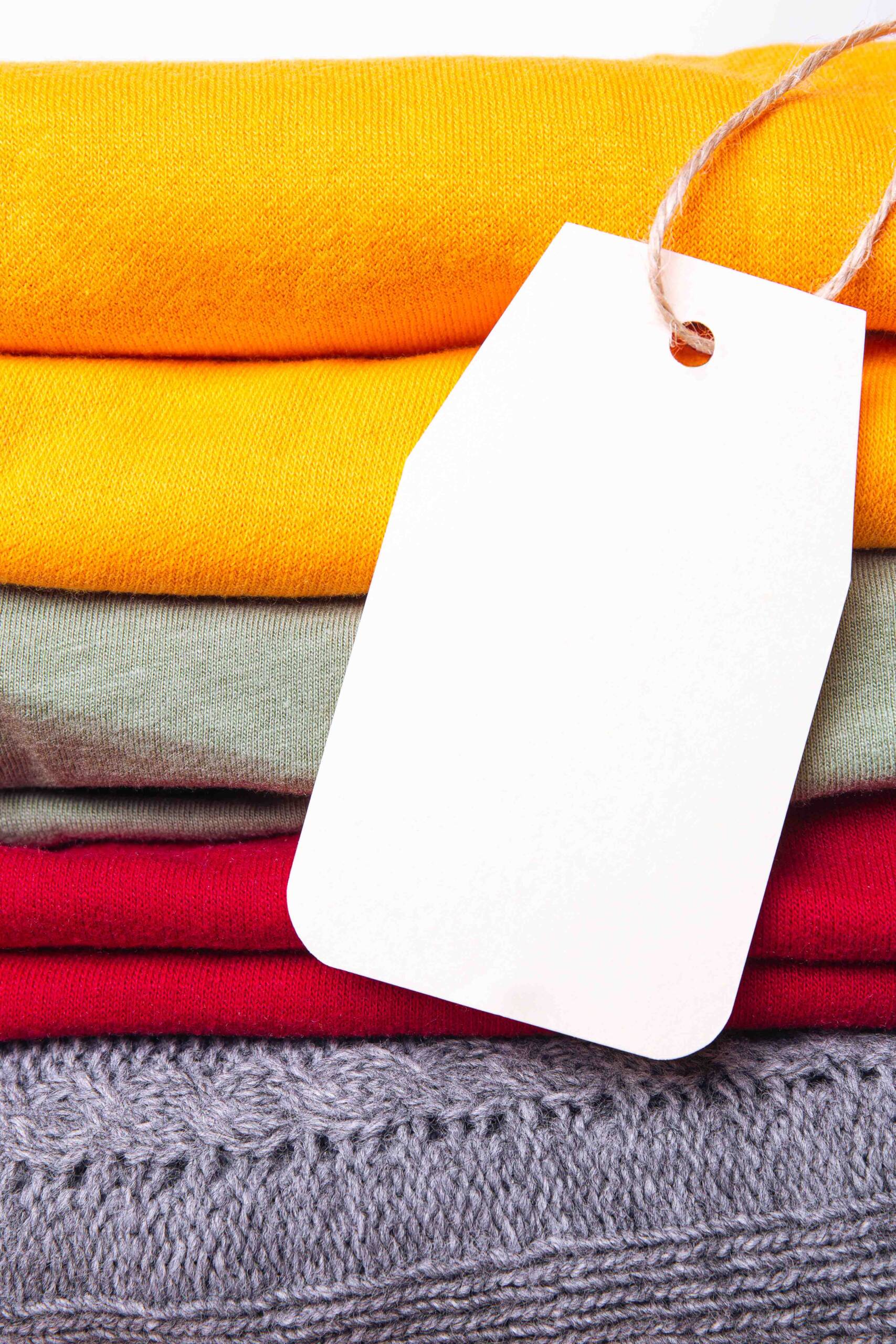 Clothes in a pile, folded in a pile of autumn bright colors with a blank label. Trending fall wardrobe colors. space for text.